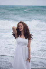 Fototapeta na wymiar Portrait of young brunette woman with curly hair in white dress smiling and enjoying sea storm in Alanya - holiday destination of Turkey
