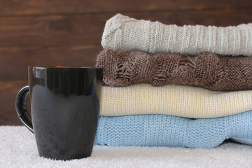 Stack of cozy knitted warm sweater and a mug of coffee . Sweater in retro style.