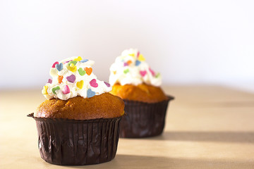 A two muffins with cream and decorative colored hearts on a light background