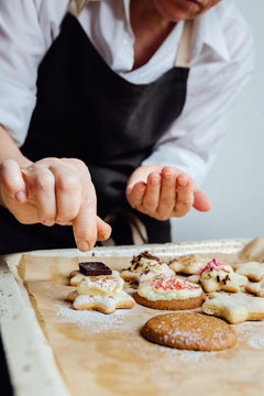 Person puts decorations on the top of the homemade cookies. Vertical studio shot. 