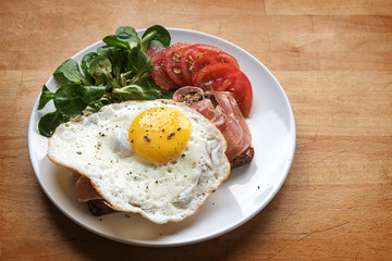 Fried egg on bread with ham, corn salad and tomatoes, wooden board with copy space
