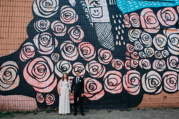 Newlyweds embracing next to graffiti wall. Young wedding couple.