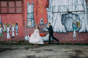 Newlyweds embracing next to graffiti wall. Young wedding couple.
