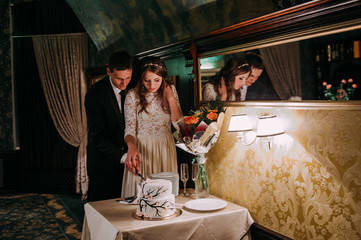 Obraz na płótnie Canvas Stylish bride and groom in the restaurant cutting cake