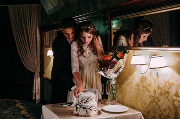 Stylish bride and groom in the restaurant cutting cake