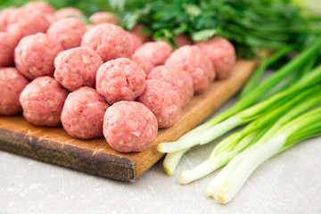 Raw meatballs on a rustic wooden cutting board on a stone backgr