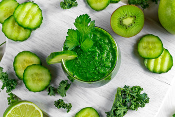 Fresh Green smoothie with kale, cucumber, lime, apple, parsley on white board.
