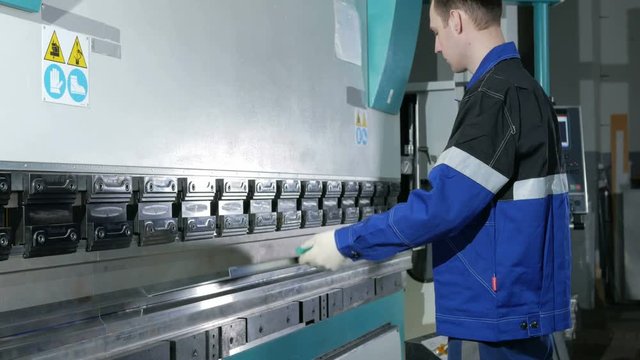 Man working with sheet metal on CNC hydraulic press brake. He puts the part and bends it into a large machine at an angle