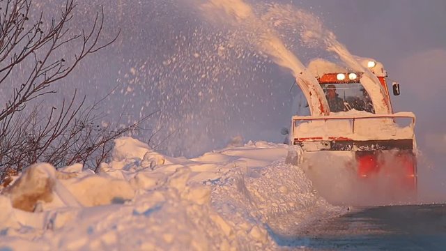 Snow truck cleaning snow from the road and streets working at sunset light on snowy day