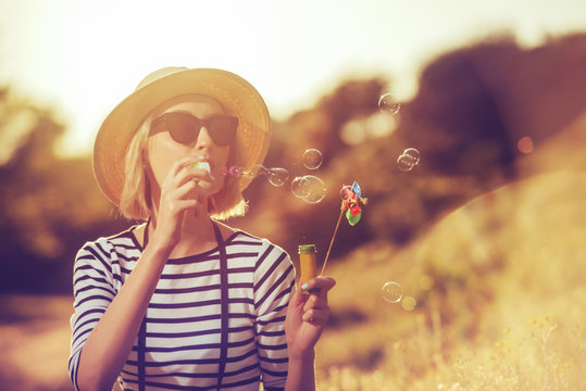 a beautiful young woman tourist is blowing soap bubbles holding a windmil toy on a sunset background