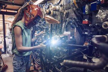 Fototapeta na wymiar woman mechanic is repairing a bicycle using electric welding 