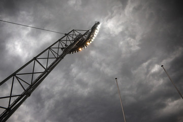 Mast of floodlights and empty flag poles against dark dramatic sky