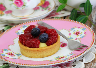 Cream cake on crunchy base with raspberries and blueberries on vintage plate, closeup
