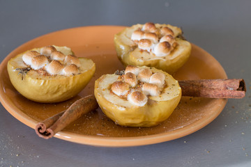 Appetizing baked apples with cottage cheese, cinnamon and marshmallows on orange plate.