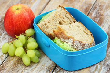 School lunch consisting of rustic bread sandwiches with cheese and lettuce, apple and grapes
