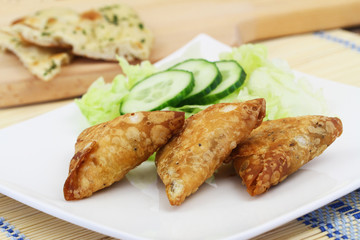 Appetizer consisting of Indian samosas with green side salad on white plate on wooden surface
