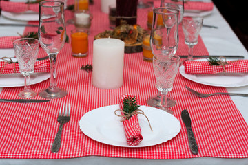 Festive composition with candles and plates. Table decoration. A beautiful table setting, red table cloth, tablecloth in a cage. Christmas dinner. A white plate with a nice napkin on the table