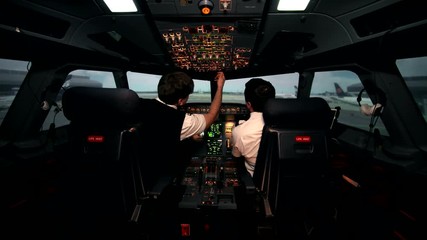 Two caucasian male pilots in the cockpit or flight deck of a passenger airplane switch controls panel of aircraft and prepare for taxiing on the runway before take off on Airbus A319 A320 A321 - Powered by Adobe