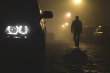 The car headlight with a walking man on the background of a fog