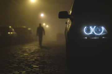 The car headlight with a walking man on a fog background. Evening-night time - obrazy, fototapety, plakaty