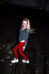 Outdoor portrait of young beautiful happy blond european lady posing on street at night. Model wearing stylish clothes red pants and jump. Female fashion. City night lifestyle. Copy space.