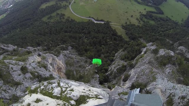 man is jumping from the cliff with green parachute