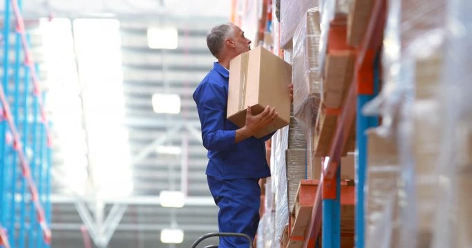 Male warehouse worker using ladder to arrange cardboard box