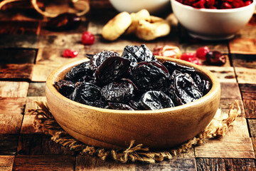 Dried sweet prunes or dark plums in bowl on wooden background, s