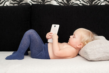 Little cute girl is playing with a smartphone, lying on the sofa