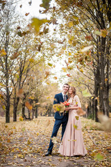 Fototapeta premium Smilng newlyweds hug under a fall of autumn leaves