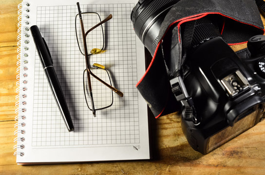 Fountain pen, camera, glasses, and notebook on a wooden table