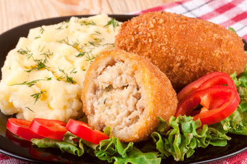 two fried breaded cutlet with mashed potatoes and lettuce on a black plate wooden background
