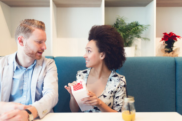 Happy middle aged multiracial couple dating. Handsome redhead man with beautiful Afro american woman having some good time in cafe bar or restaurant. Woman receiving gift from man.
