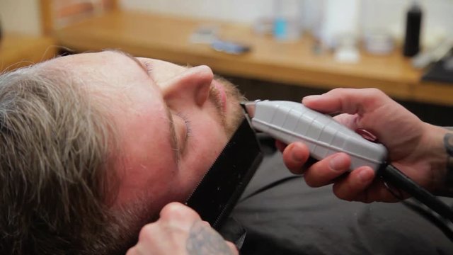 Barber cuts the hair of the client with clipper at barbershop.