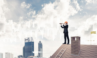 Engineer man standing on roof and looking in spyglass. Mixed med