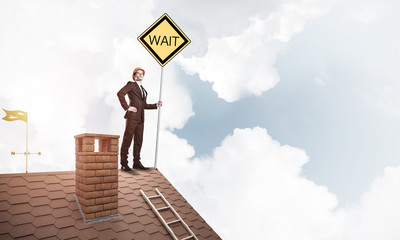 Young businessman on house brick roof holding yellow signboard. 