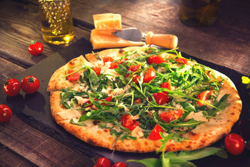 Pizza Caprese with arugula, cheese, yoghurt and cherry tomatoes. Homemade delicious vegetarian pizza on wooden table