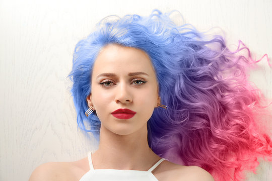 Trendy hairstyle concept. Young woman with colorful dyed hair on white wooden background