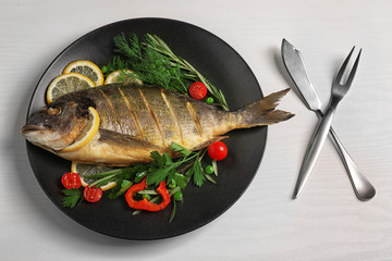 Tasty fish with vegetables on plate on white wooden table