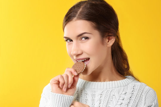 Pretty Young Woman Eating Tasty Cookie, On Yellow Background