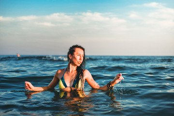 Beautiful young brunette woman in the sea at sunset