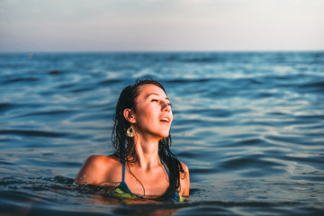 Beautiful young brunette woman in the sea at sunset