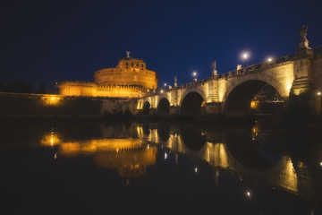 Fototapeta na wymiar Puente hacia el Castillo de San't Angelo, de noche con iluminación de farolas y con reflejos en el río Tiber. Roma, Italia