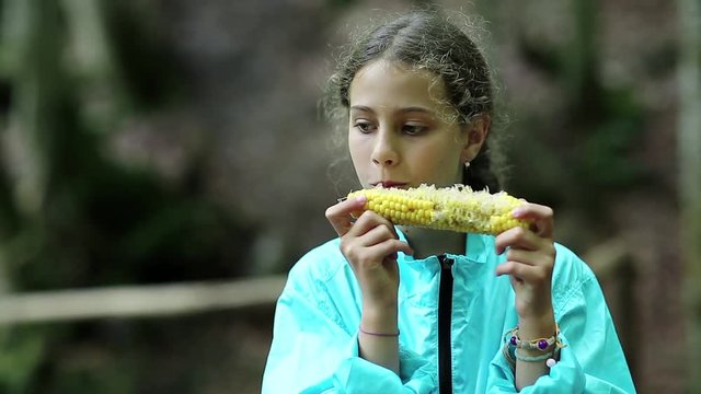 Girl eats corn. Beautiful girl in blue jacket eats corn and looks around. Female with corncob