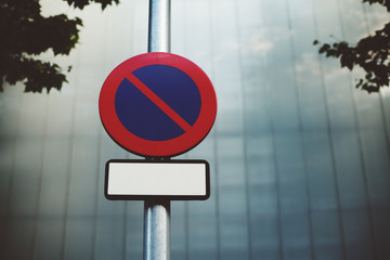 "No parking" road sign with blank frame for your text placed on metal street lantern, blurred tiled facade of building in background