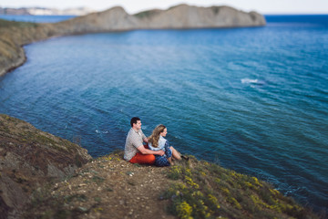 Fototapeta na wymiar Couple relaxing by the sea with amazing mountain view. Jeans jacket and blue skirt