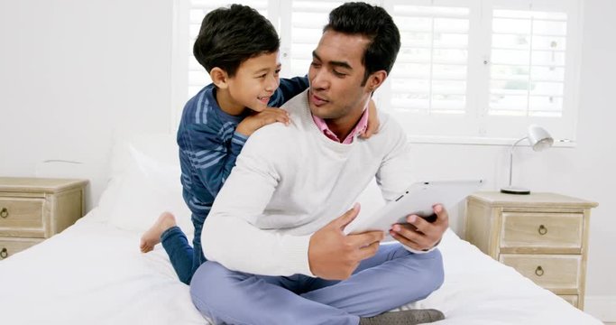 Father and son using digital tablet on the bed