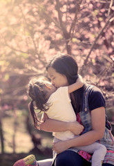 Mother kiss and hug daughter in the pink flower background