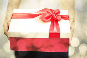 Hands holding red gift or present box with red ribbon and bokeh