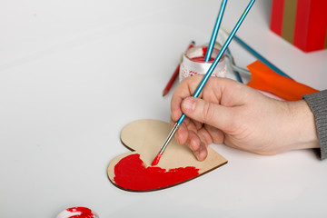 Love prepares suaenir Valentine's Day. To paint a wooden heart with red paint brush.